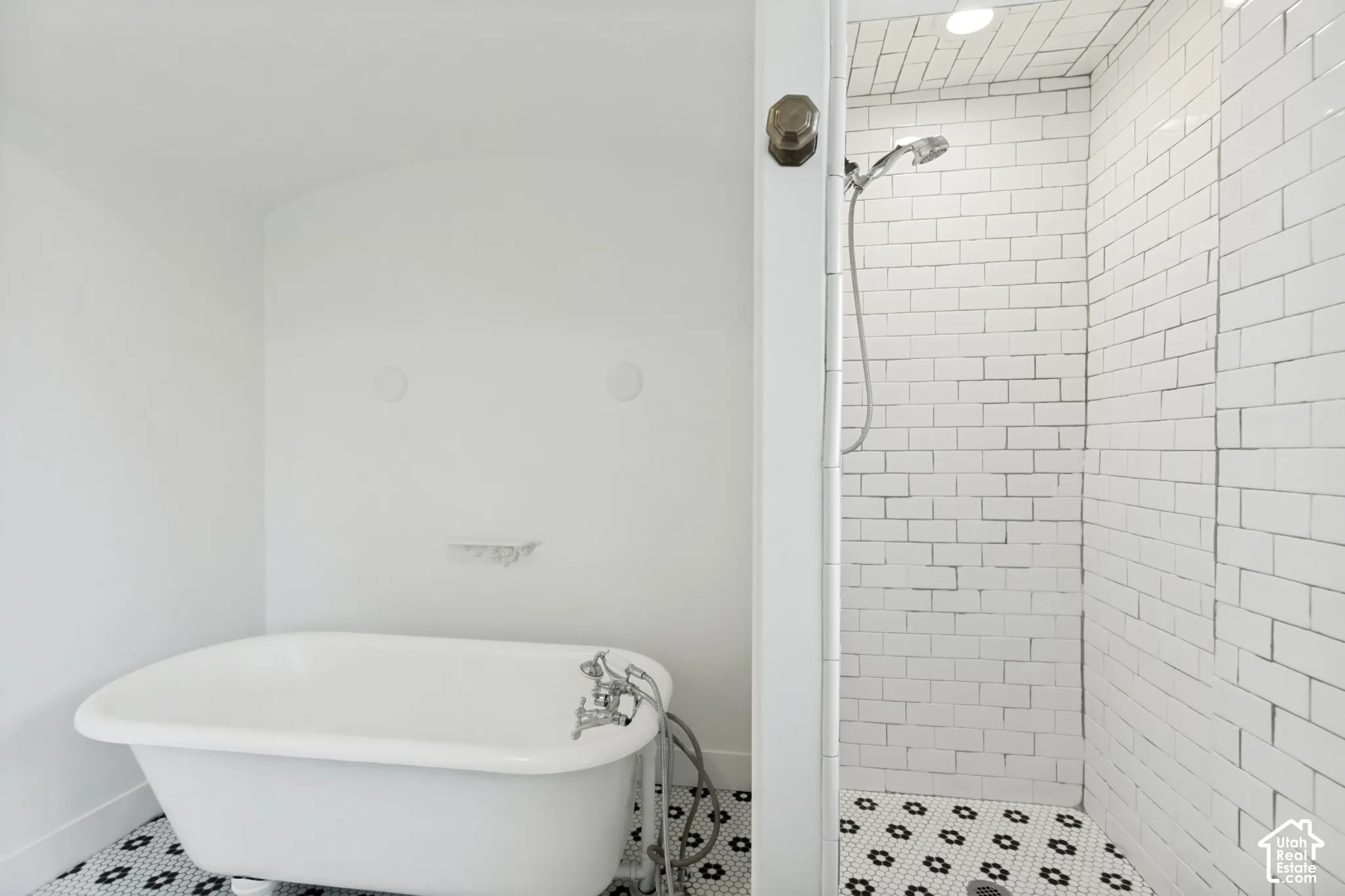 Freestanding clawfoot tub with metallic faucet, walk-in shower featuring subway tile surround, and black-and-white geometric mosaic floor tile