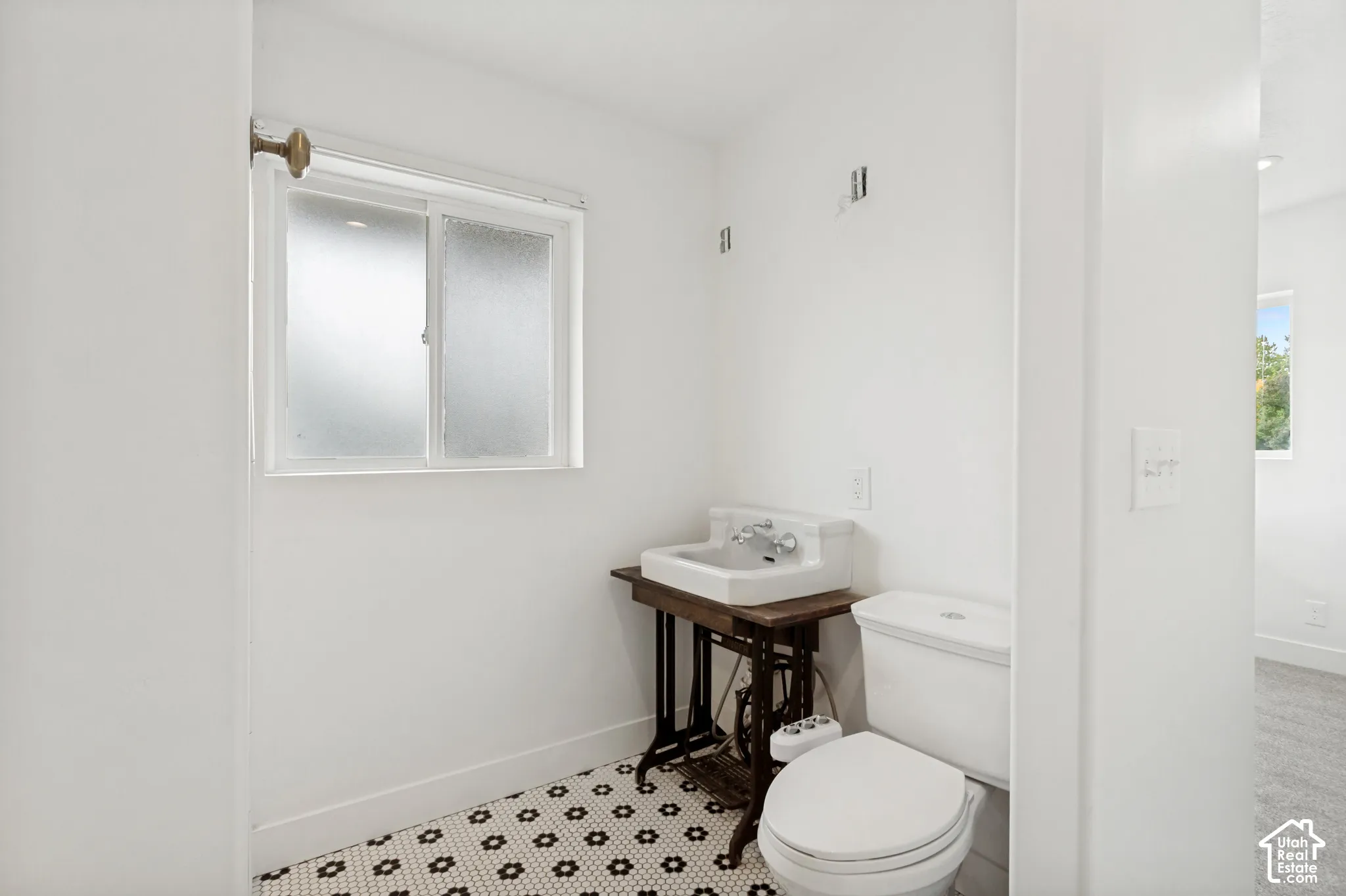 Bathroom featuring white wall-mounted basin, vintage-style iron base, frosted slider window, and geometric patterned tile flooring