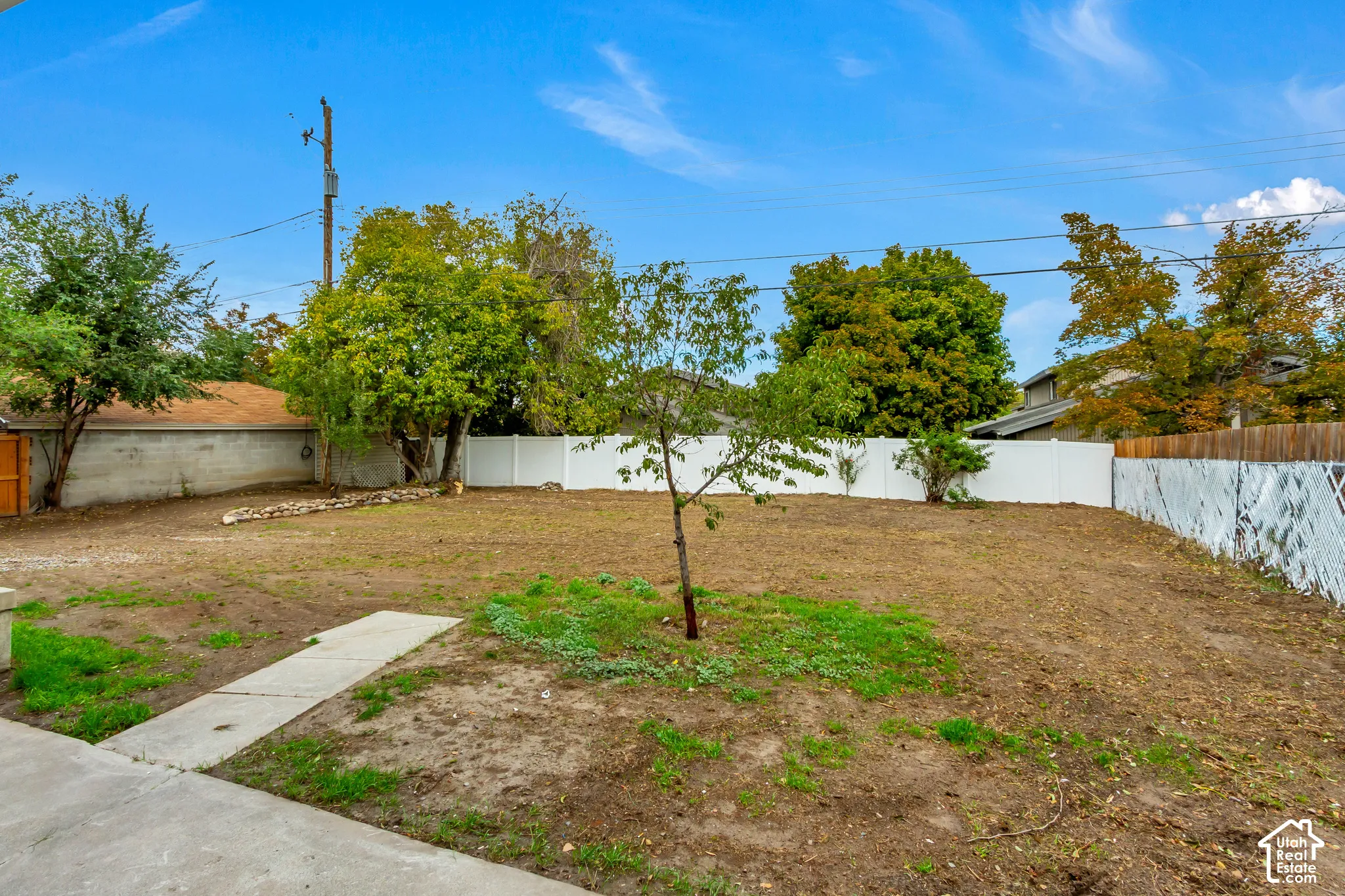 Expansive backyard featuring a white vinyl privacy fence, concrete patio, mature trees, and open grounds