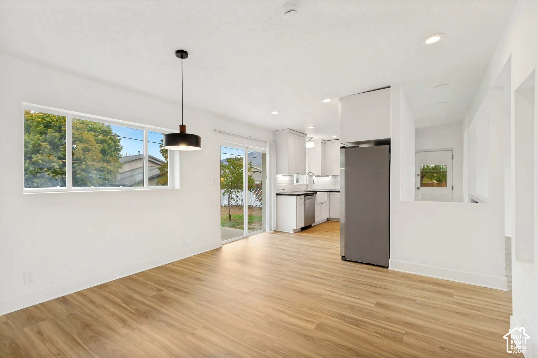 Open-concept space featuring wood-finish flooring, recessed lighting, a modern pendant light fixture, stainless steel kitchen appliances, and sliding glass doors