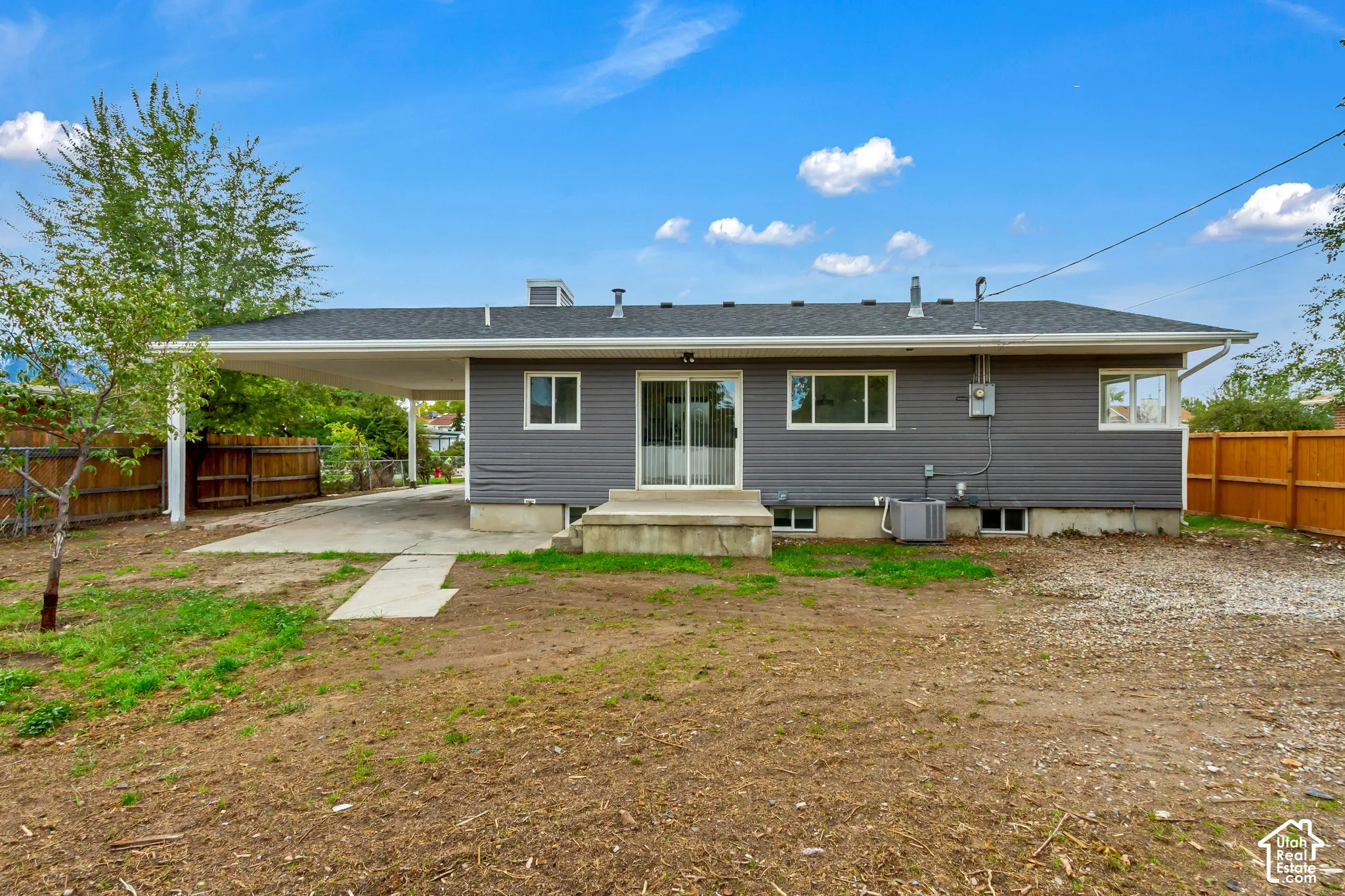 Single-story residence featuring horizontal siding, a covered carport, a concrete rear patio, sliding glass doors, and a wood privacy fence