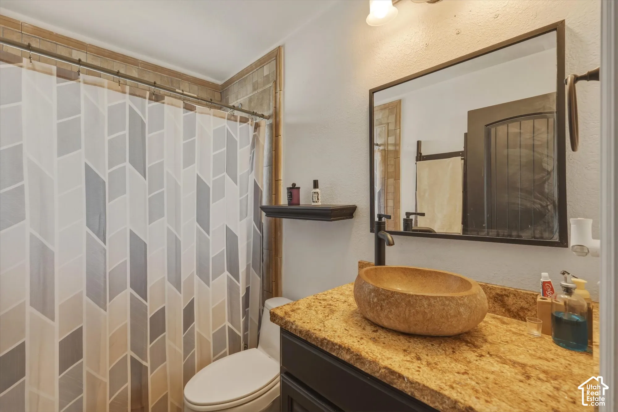 Vanity featuring a vessel sink, stone-finish countertop, dark cabinetry, framed mirror, and matte black hardware, accompanied by tiled shower enclosure