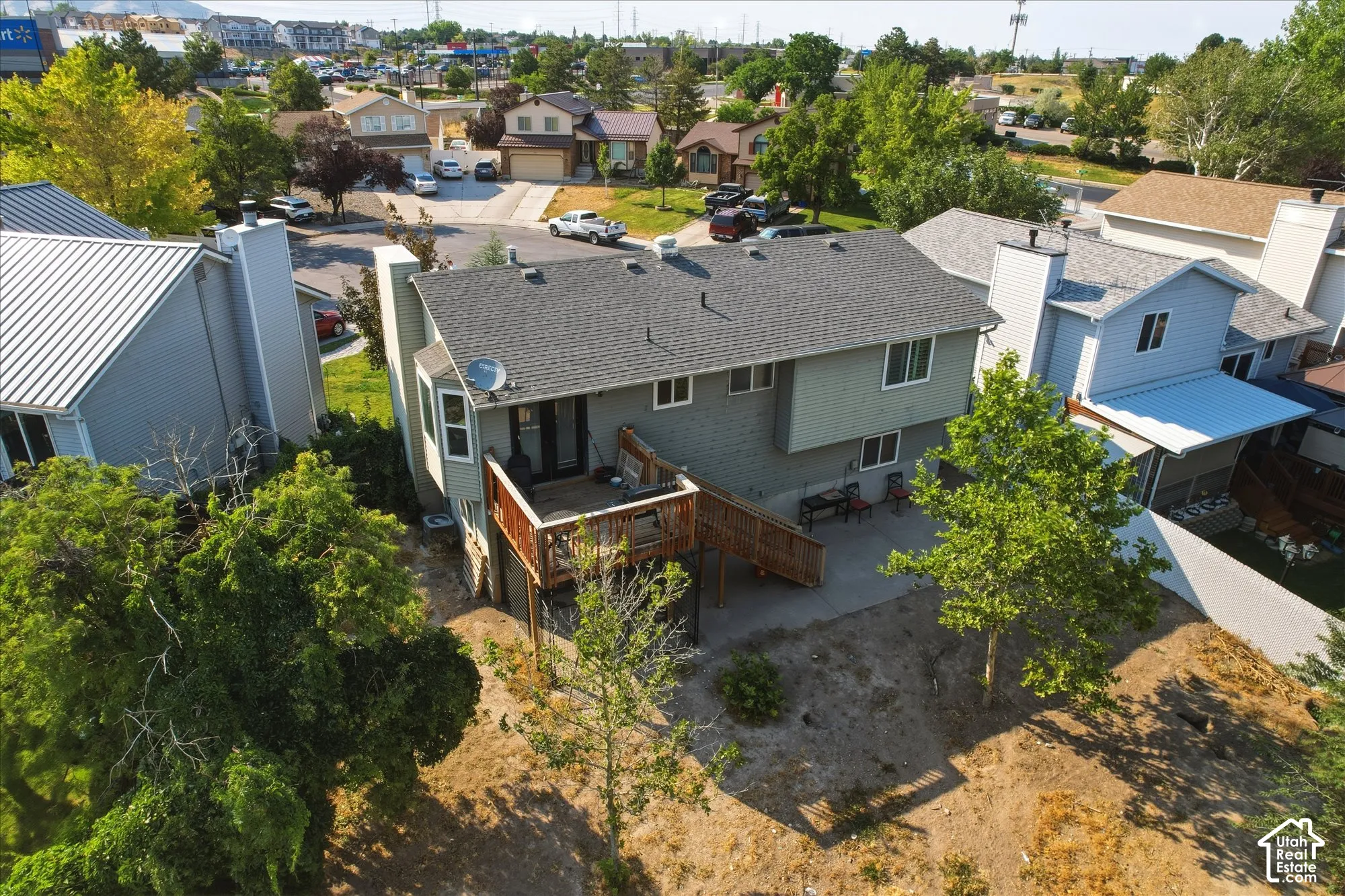 Multi-level residence featuring an elevated wooden deck, lower-level concrete patio, horizontal siding, and mature trees on the property