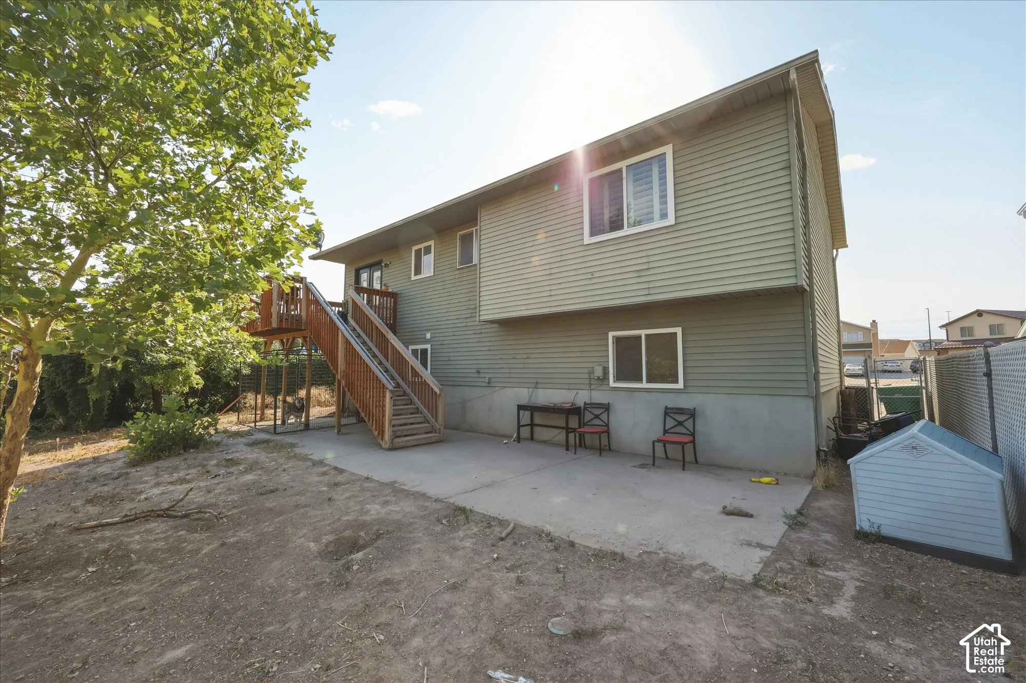 Exterior facade featuring horizontal siding, a raised wood deck with staircase, concrete patio, and fenced perimeter