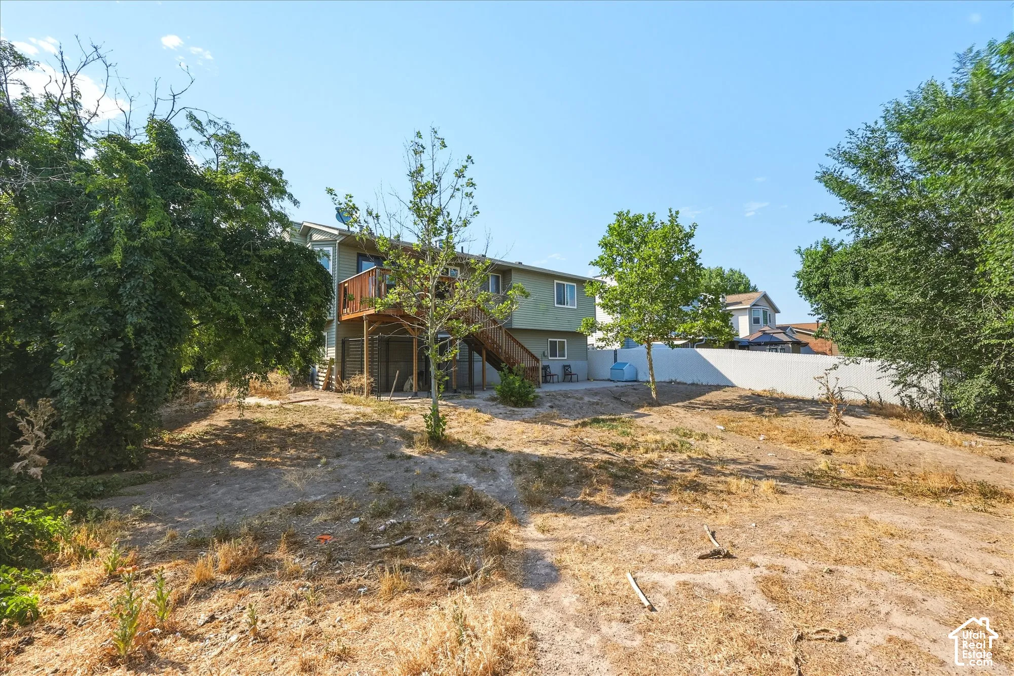 Exterior of residence featuring a raised wood deck, paved patio area, and a white privacy fence