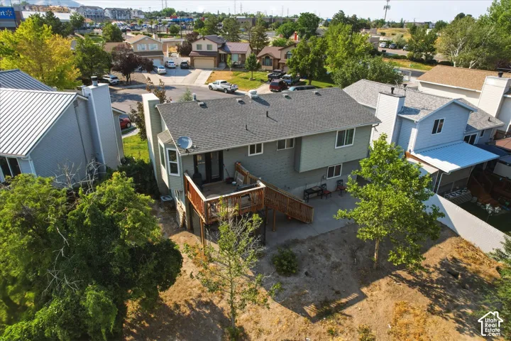 Multi-level residence featuring an elevated wooden deck, lower-level concrete patio, horizontal siding, and mature trees on the property