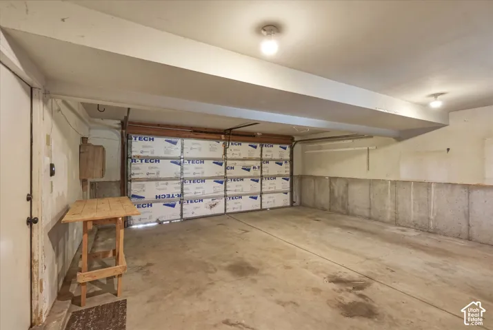 Enclosed garage featuring concrete flooring, exposed poured concrete walls, ceiling-mounted lighting, and an insulated sectional door