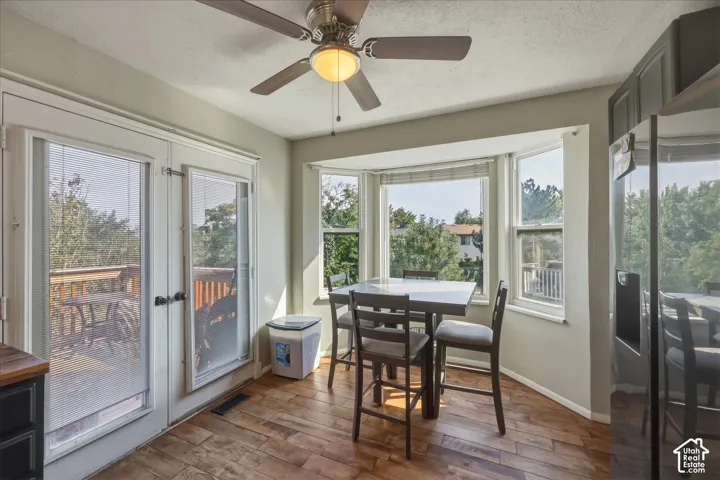 Breakfast nook featuring wood-finish flooring, bay windows, and a ceiling fan with integrated lighting, paired with full-light glass panel doors