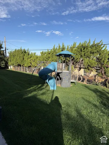 Expansive lawn area featuring a metal chain-link perimeter fence, mature evergreen trees