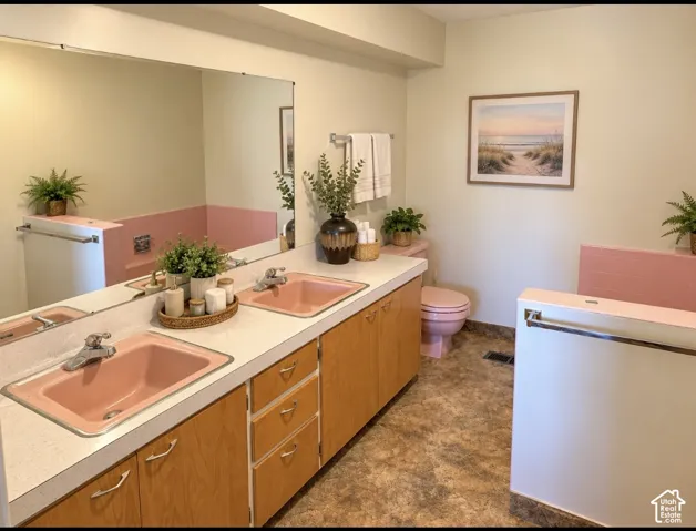 Dual-sink vanity with light-tone wood cabinetry, solid-surface countertop, integrated basin sinks, and expansive wall-mounted mirror