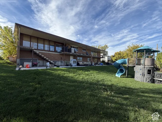 Brick exterior with a metal staircase, covered balcony, concrete patio, and sloped lawn