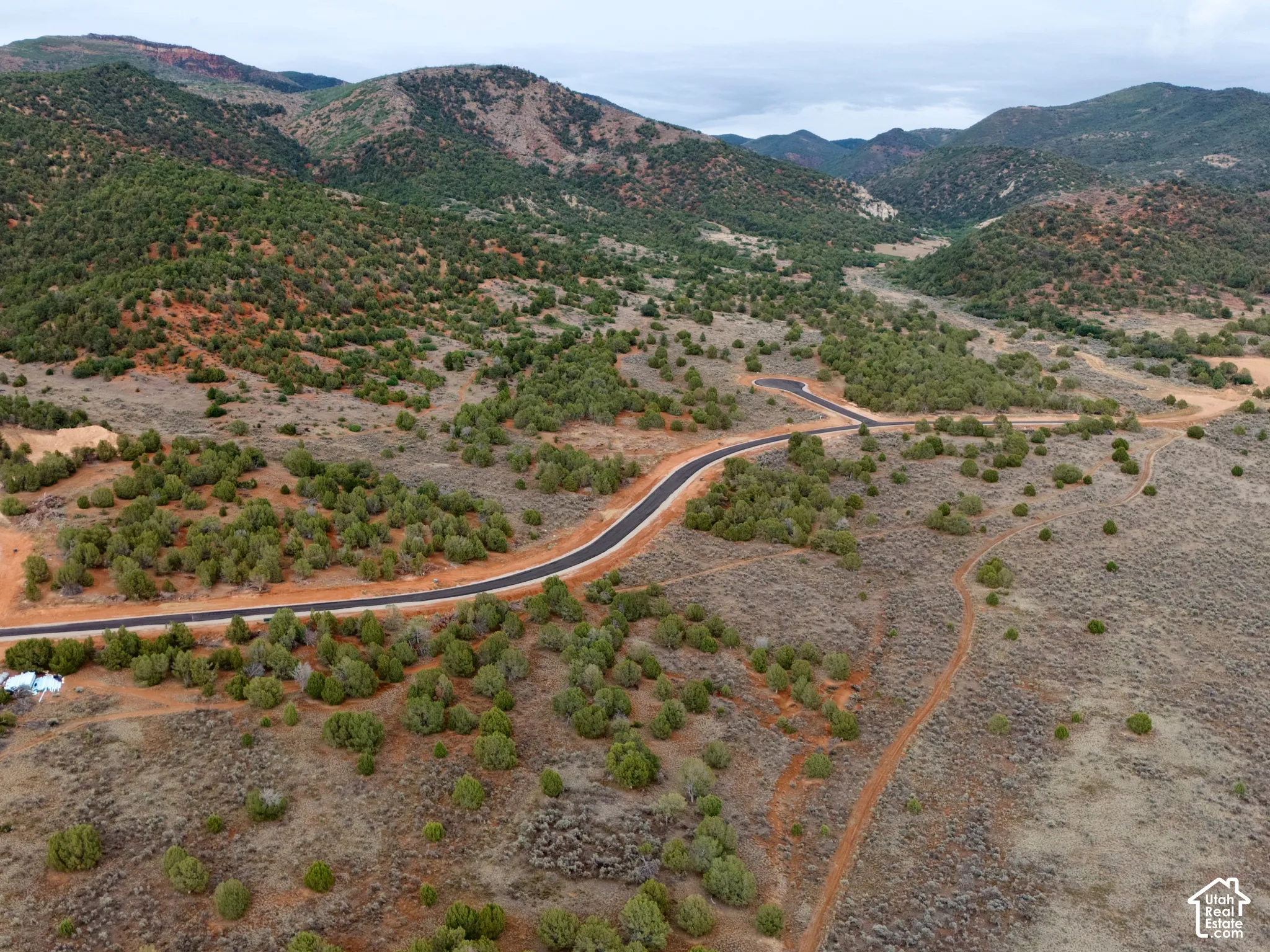 Expansive undeveloped land featuring paved asphalt roadways, native desert vegetation, rolling terrain, and a mountainous backdrop