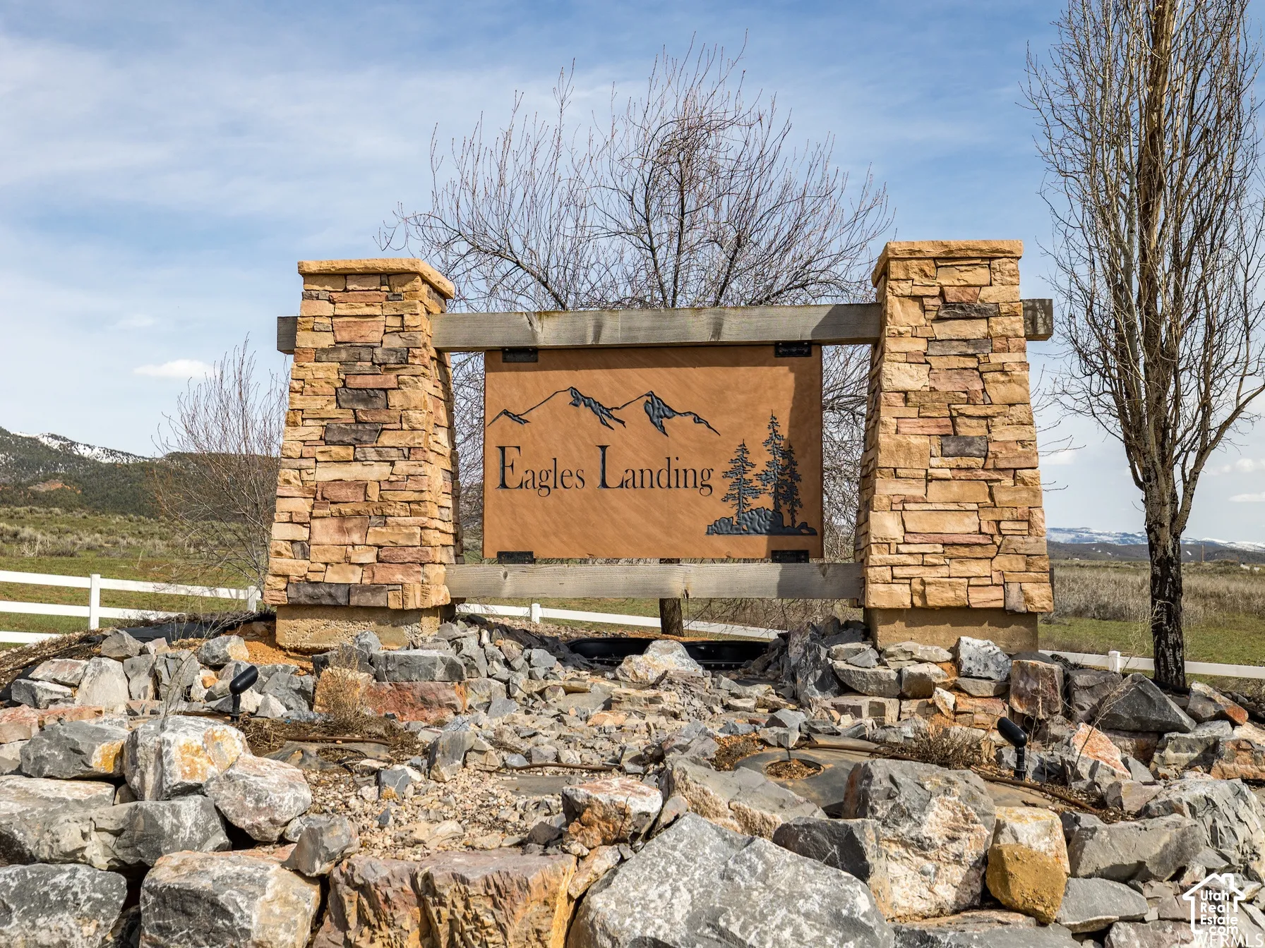 Community monument sign featuring dual stacked-stone pillars, timber framing, and metallic signage set against a mountain backdrop