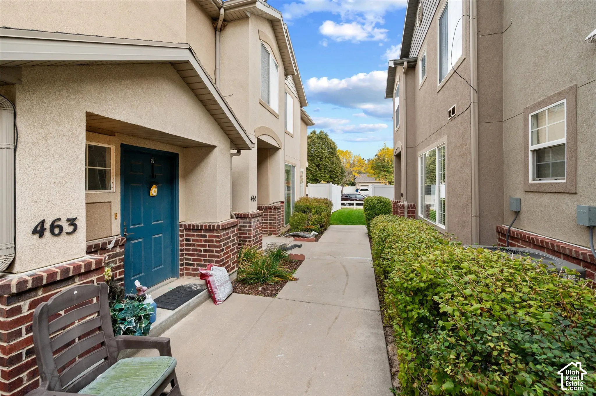 Exterior featuring stucco siding, multi-toned brick masonry accents, a recessed entryway with a solid door, and a concrete walkway bordered by manicured hedging