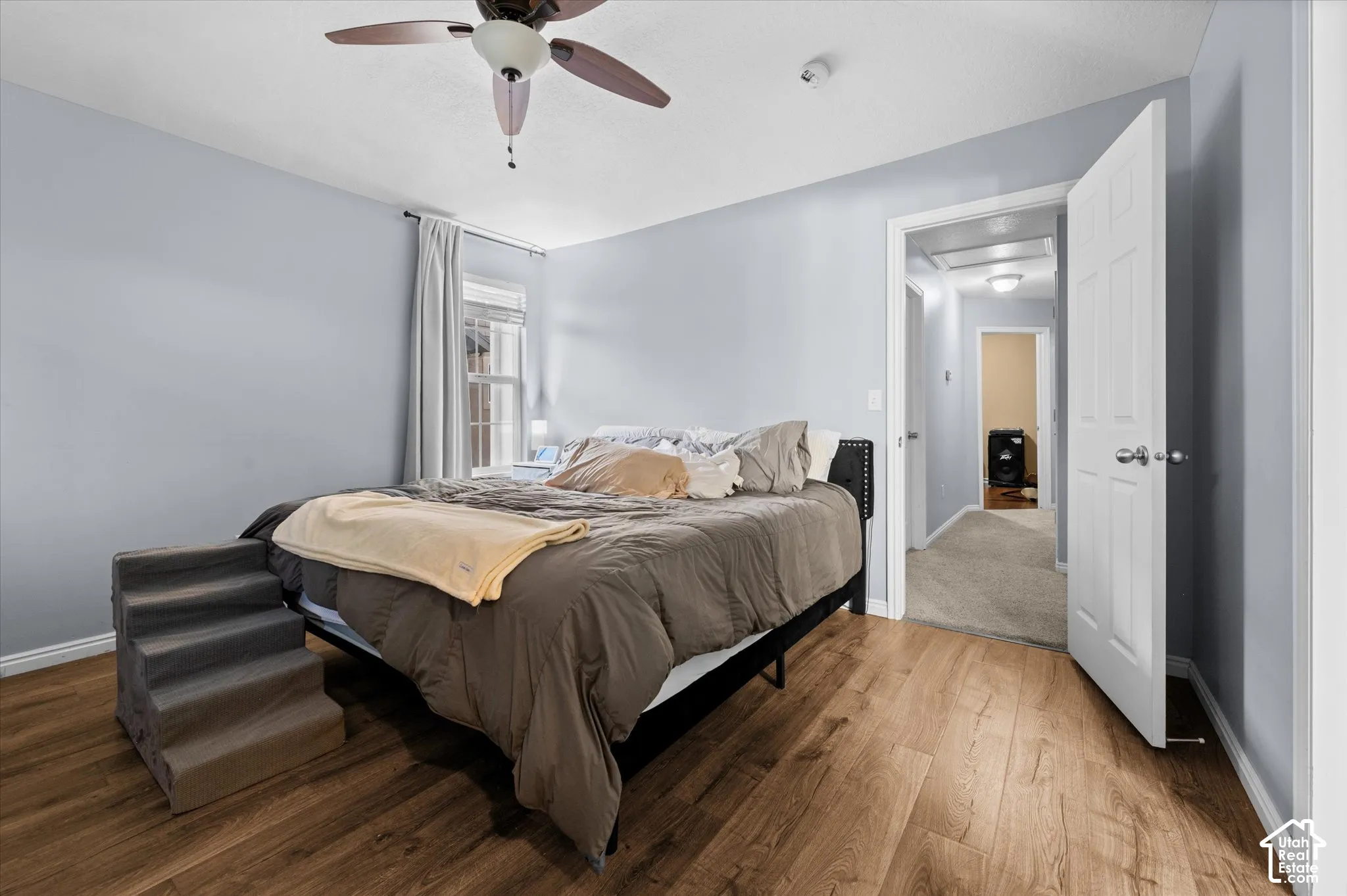 Room featuring wood-finish flooring, a ceiling fan with integrated lighting, and a six-panel interior door