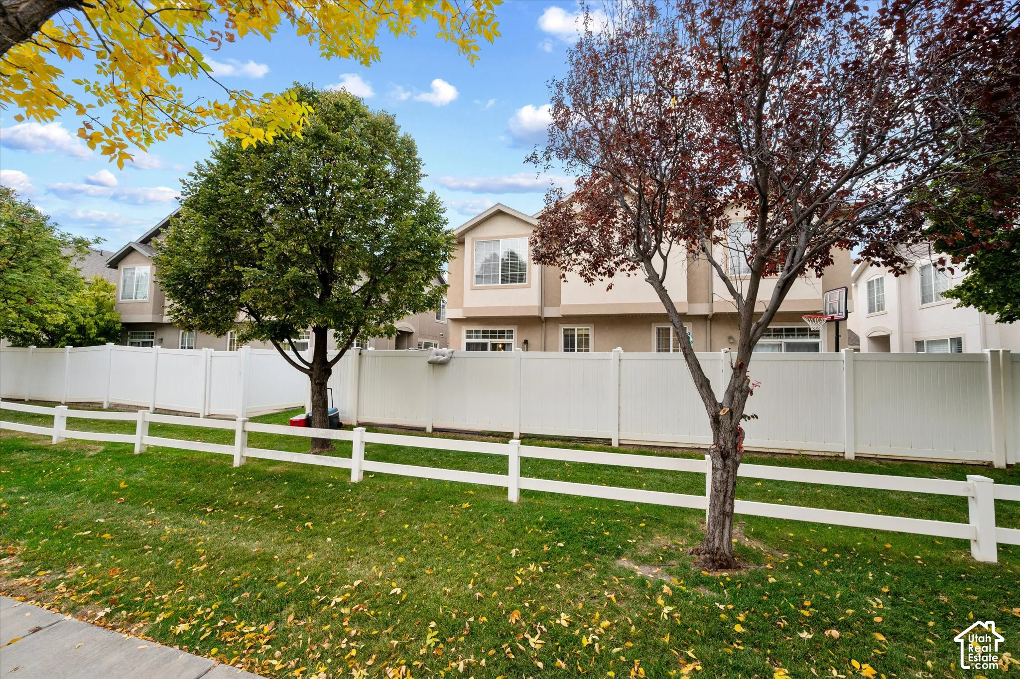 Exterior of the property featuring a white vinyl privacy fence, a low-profile white rail fence, and mature trees on the premises