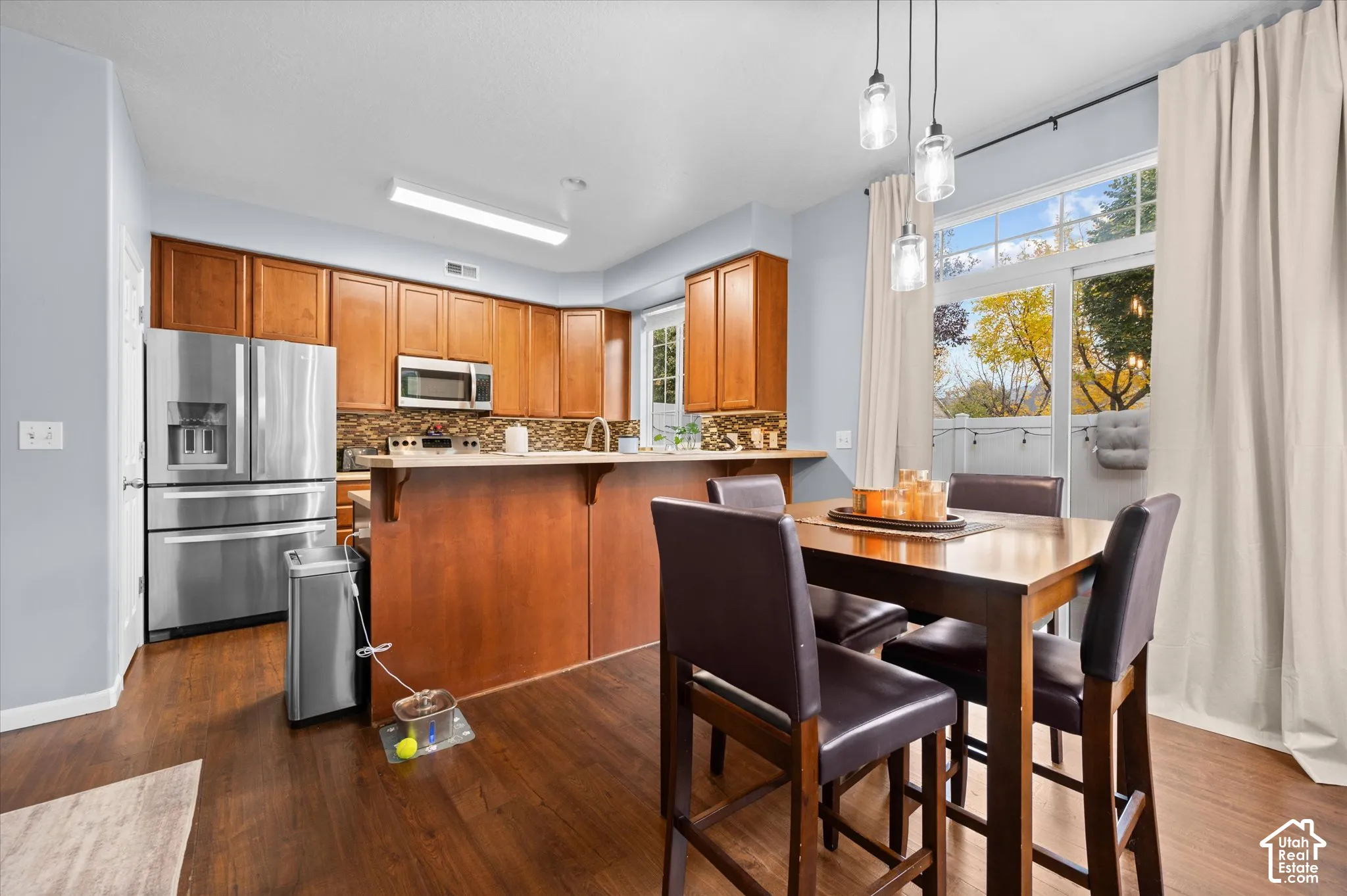 Kitchen featuring wood cabinetry, stainless steel appliances, a tile backsplash, wood-finish flooring, and a breakfast bar