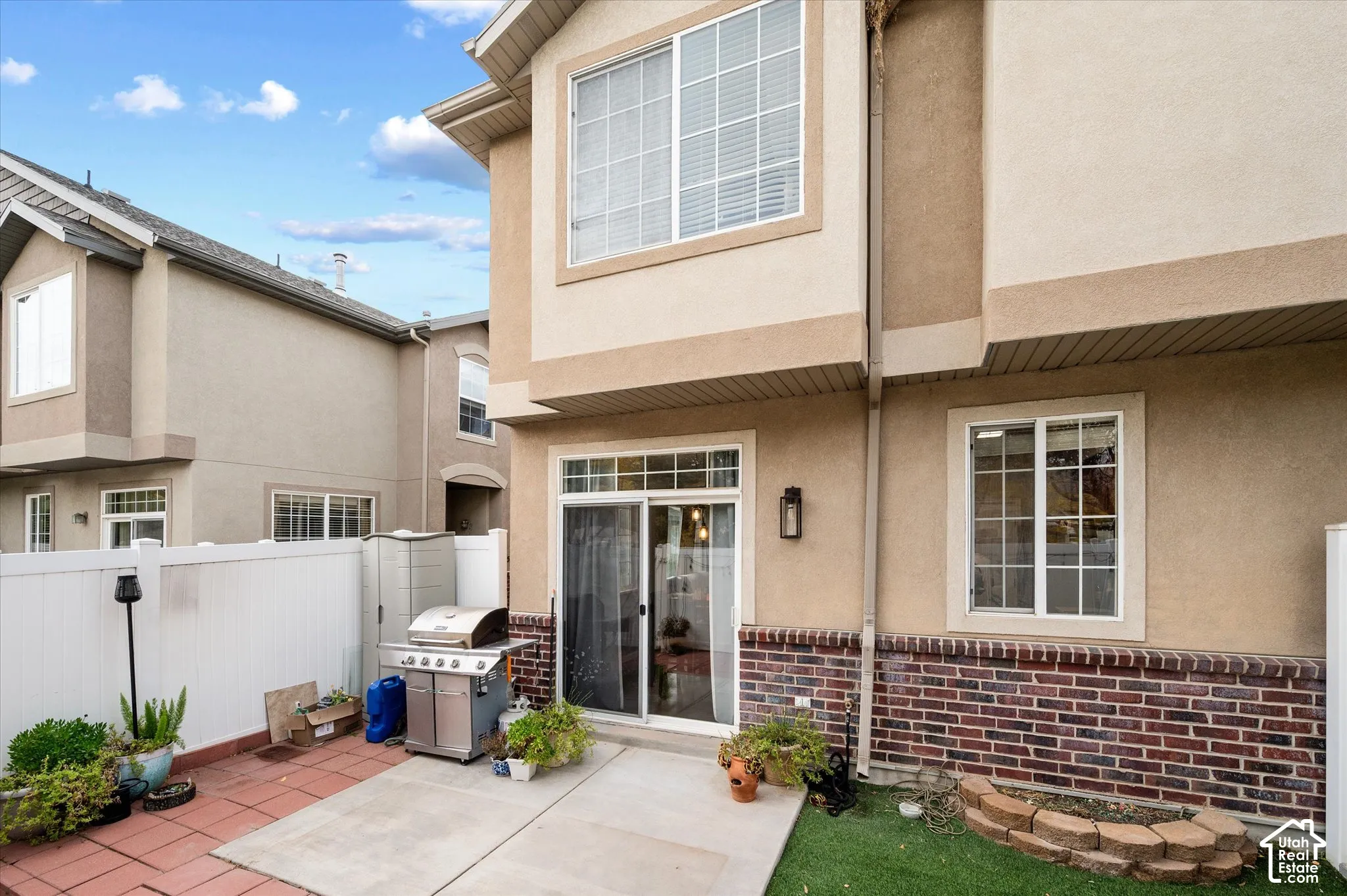 Exterior elevation featuring a multi-tone stucco finish, red brick lower masonry, sliding glass patio door, and white vinyl privacy fencing