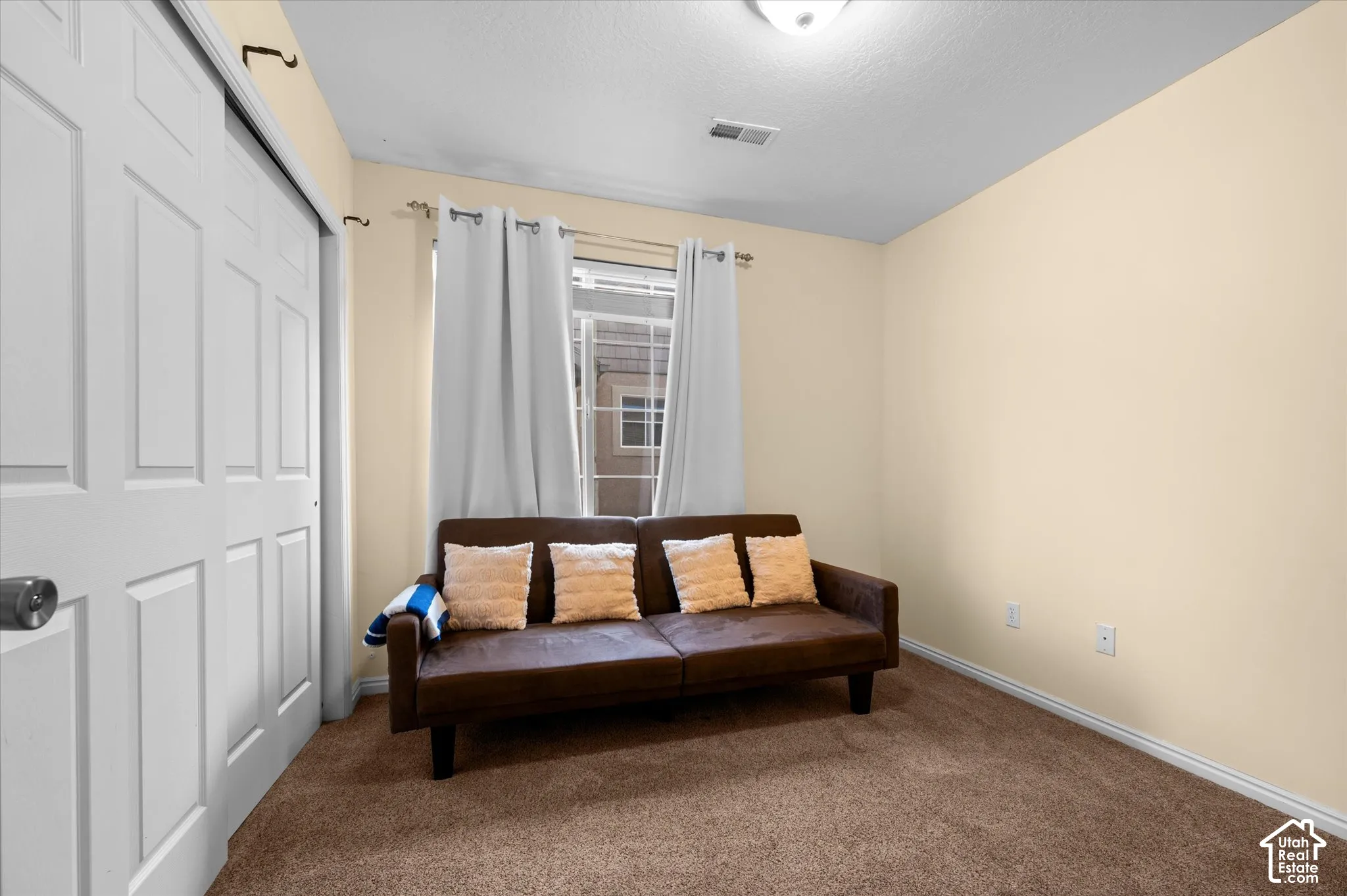Neutral-toned interior featuring wall-to-wall carpeting, a dual-panel sliding closet door, and a single-hung window with a metal curtain rod