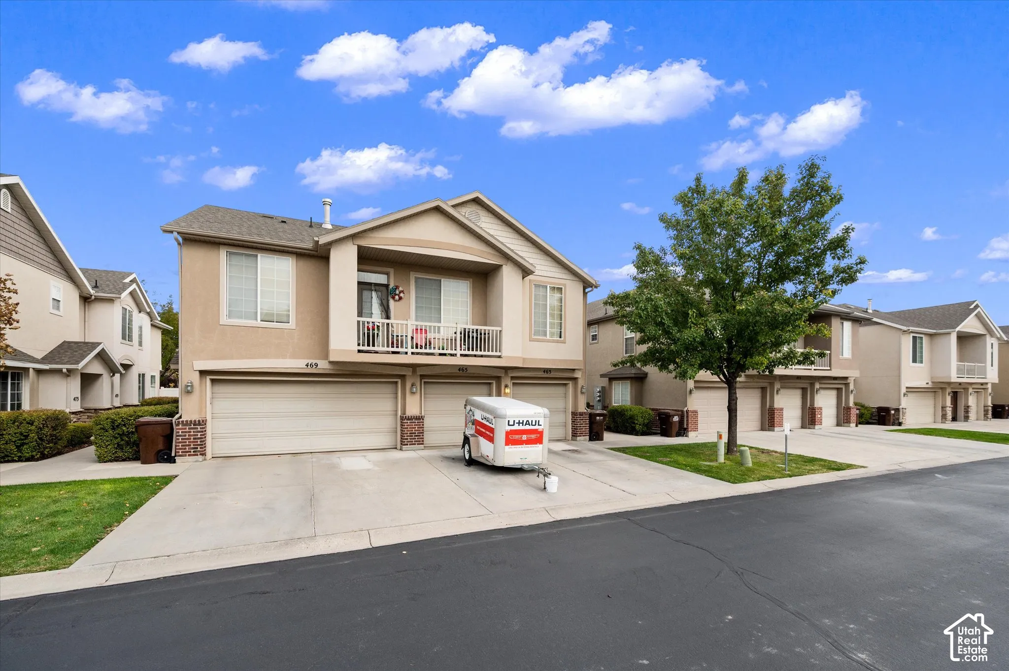 Multi-level stucco exterior featuring a three-car garage, second-story balcony, and shingled roof