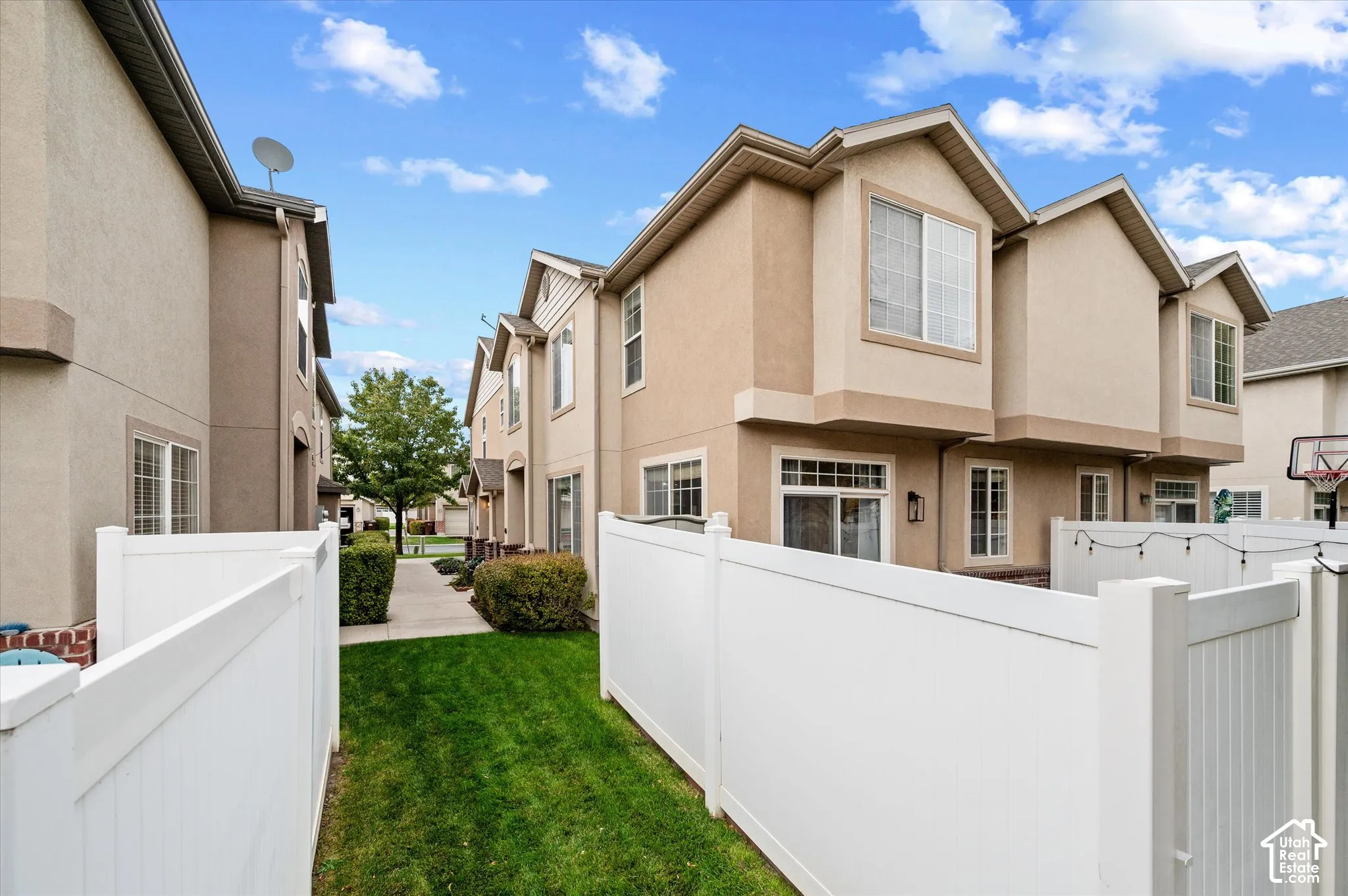Multi-level exterior featuring stucco siding, gabled rooflines, vinyl privacy fencing, and a manicured lawn