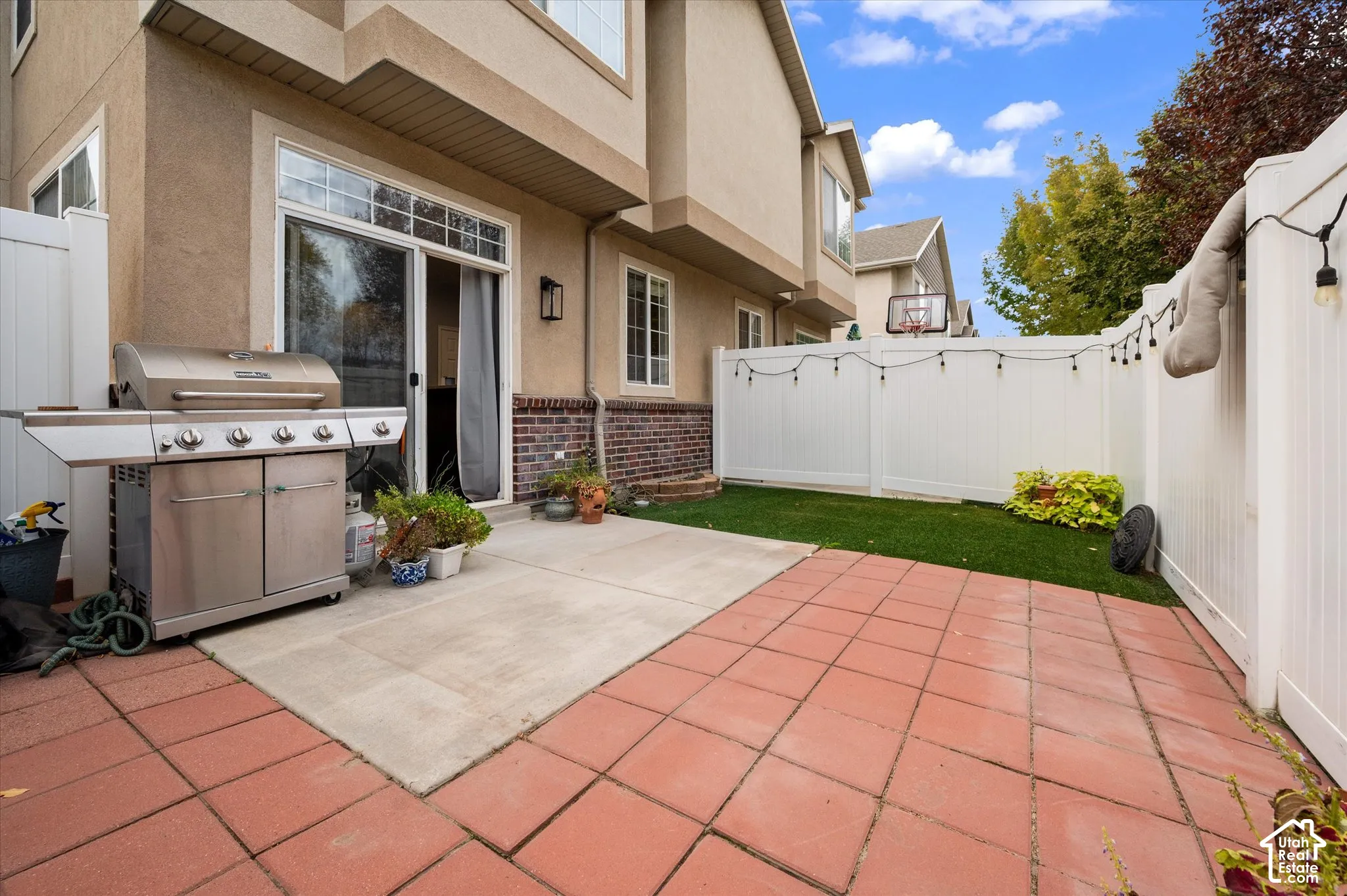 Fenced backyard featuring a paved patio, synthetic turf area, and integrated brick masonry exterior wall detail