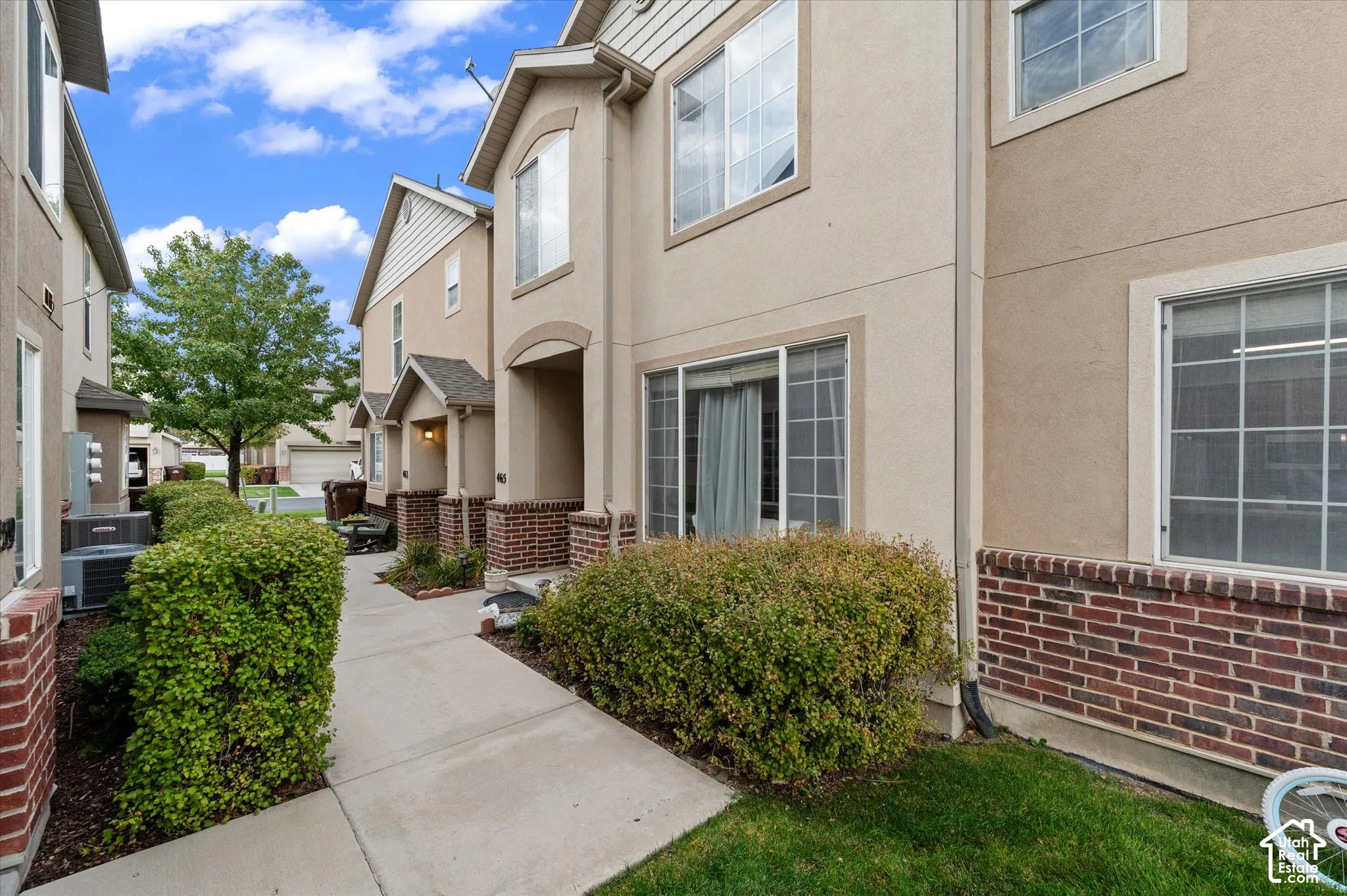 Multi-story exterior featuring a stucco facade, red brick accents, concrete walkway, and window grids