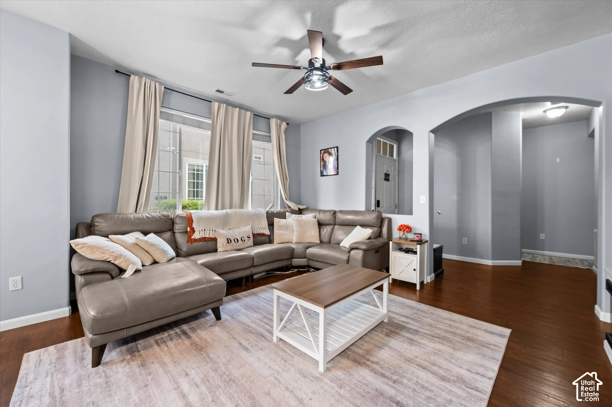 Living area featuring wood-finish flooring, arched architectural detailing, and a multi-blade ceiling fan with integrated lighting