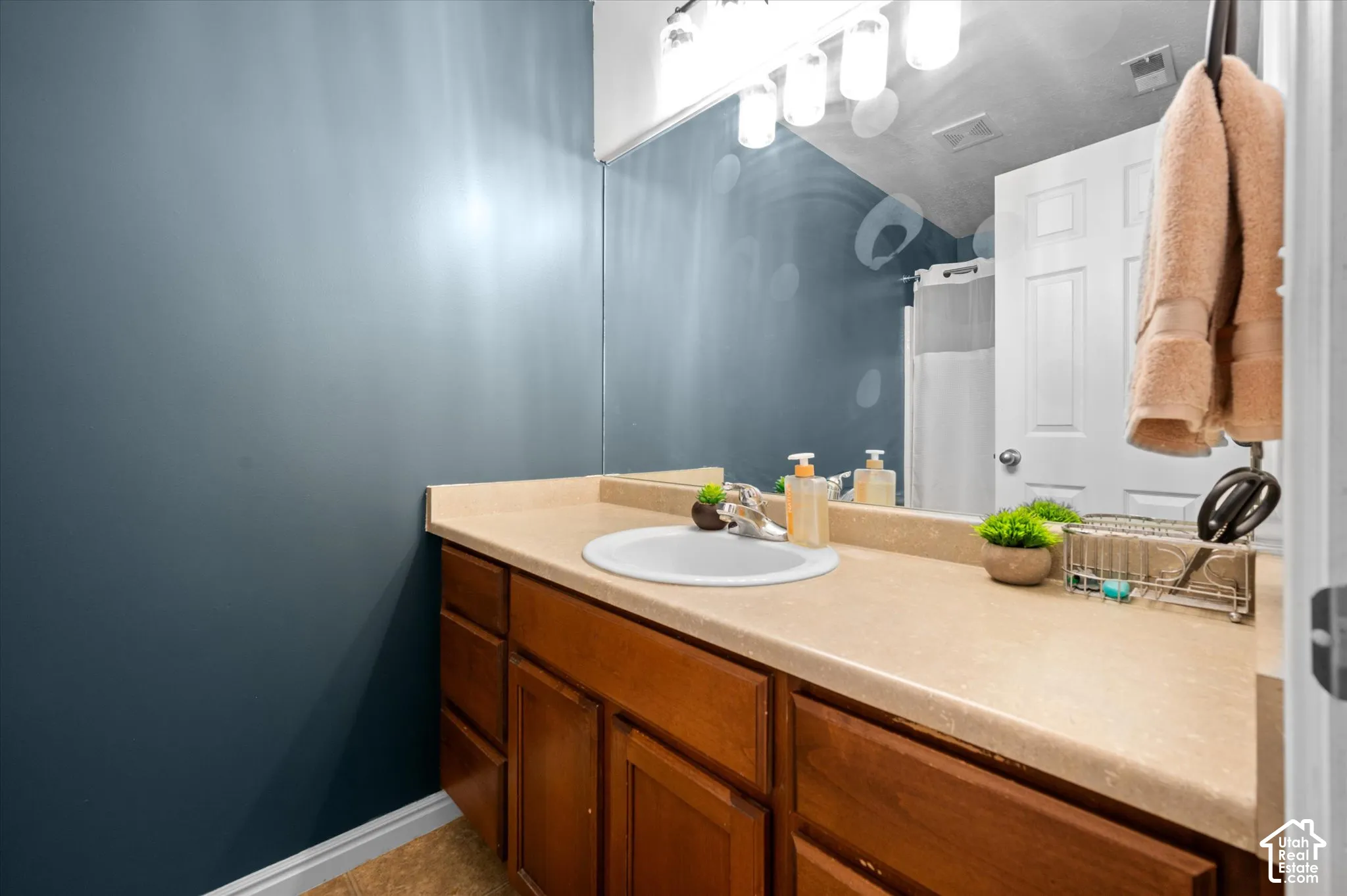Vanity featuring a solid surface countertop, integrated oval sink, chrome faucet, and wood-finish cabinetry topped by a full-width wall mirror and four-bulb overhead lighting fixture