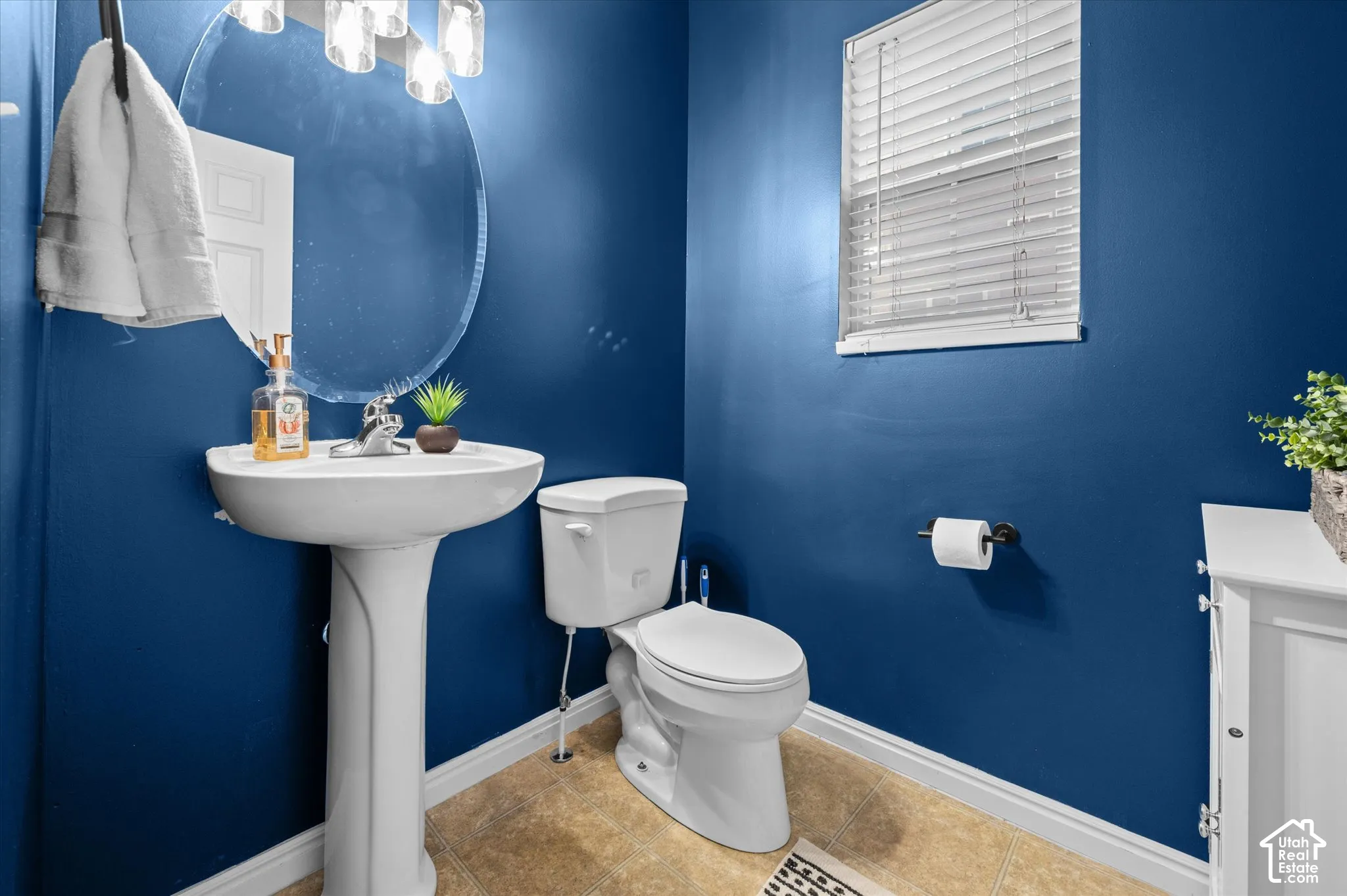 Pedestal sink with polished chrome faucet, round frameless mirror, multi-bulb overhead vanity lighting, and ceramic tile flooring