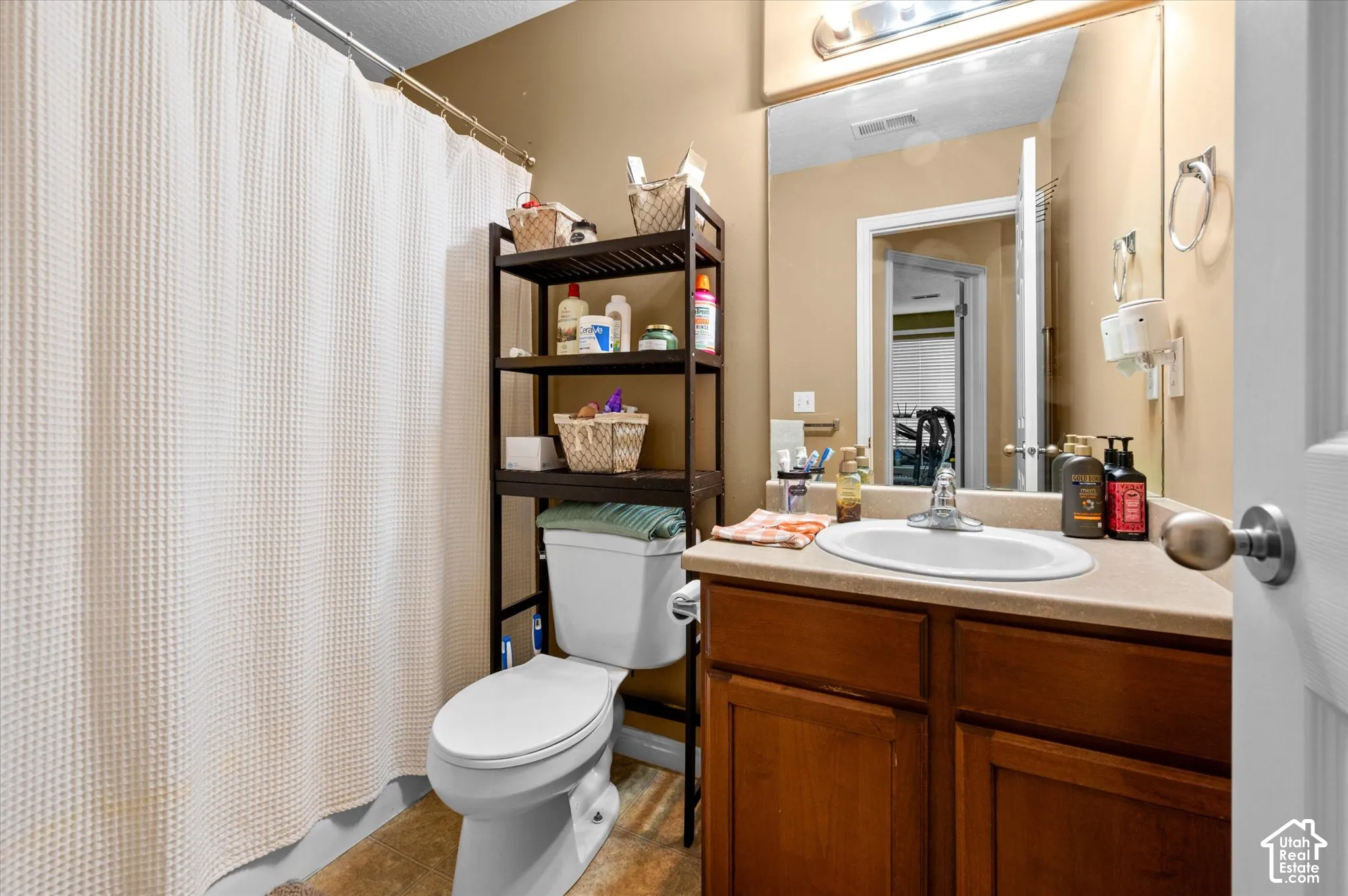 Bathroom featuring a wood-finish vanity with a stone-composite countertop, integrated oval basin, full-width vanity mirror, and polished-finish hardware