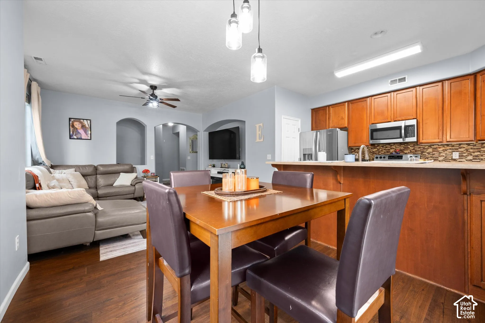 Open concept area featuring wood-finish flooring, wood cabinetry, stone-style tile backsplash, pendant lighting, and arched wall insets