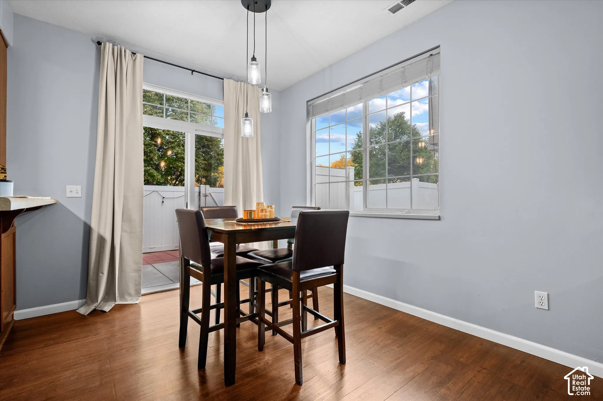 Dining area featuring wood-finish flooring, a multi-light pendant fixture, large windows with muntin bars, and a sliding glass door providing external access