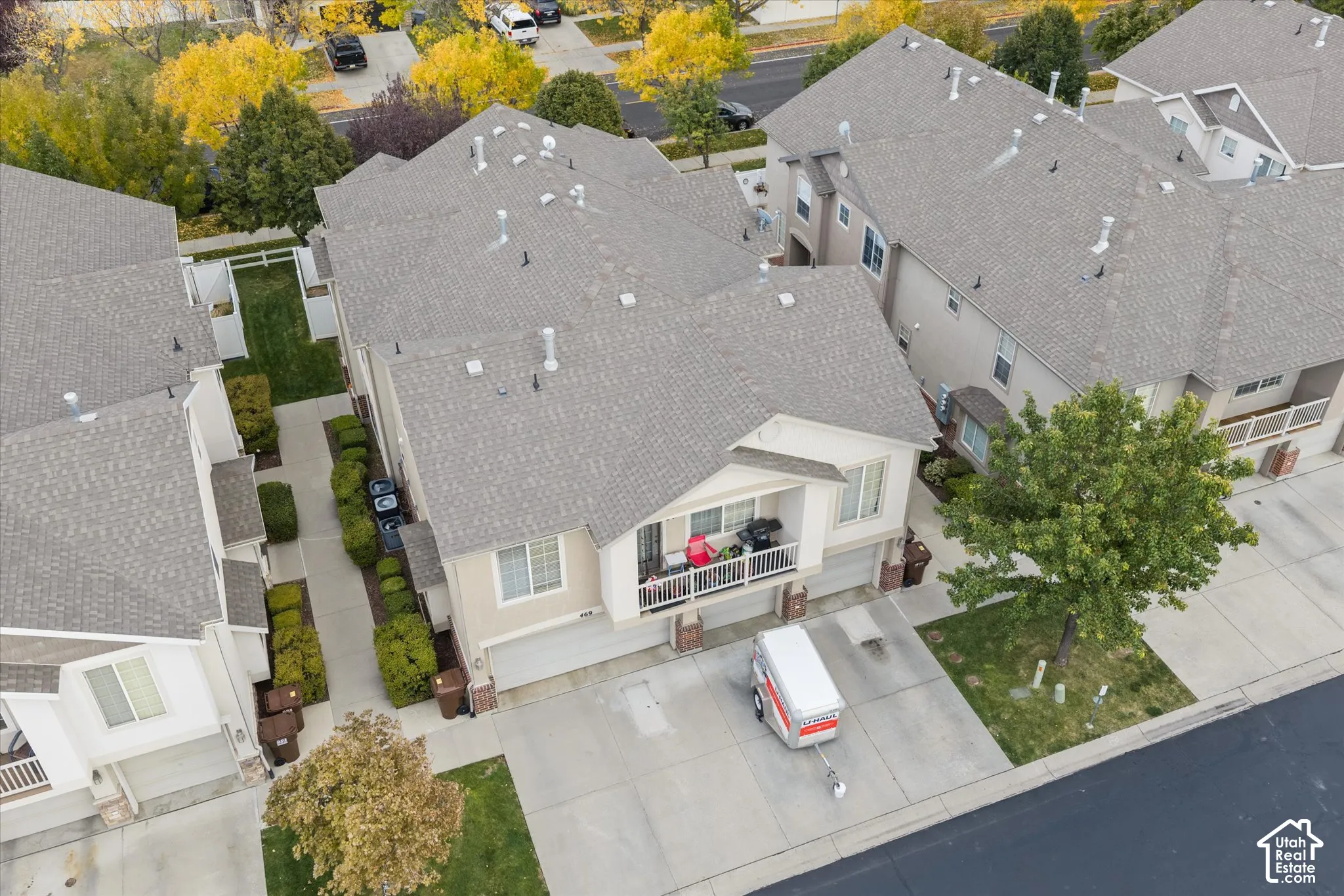 Aerial perspective of multi-level residential structure featuring a shingled roof, stucco siding, concrete driveway, and a covered balcony with a white railing