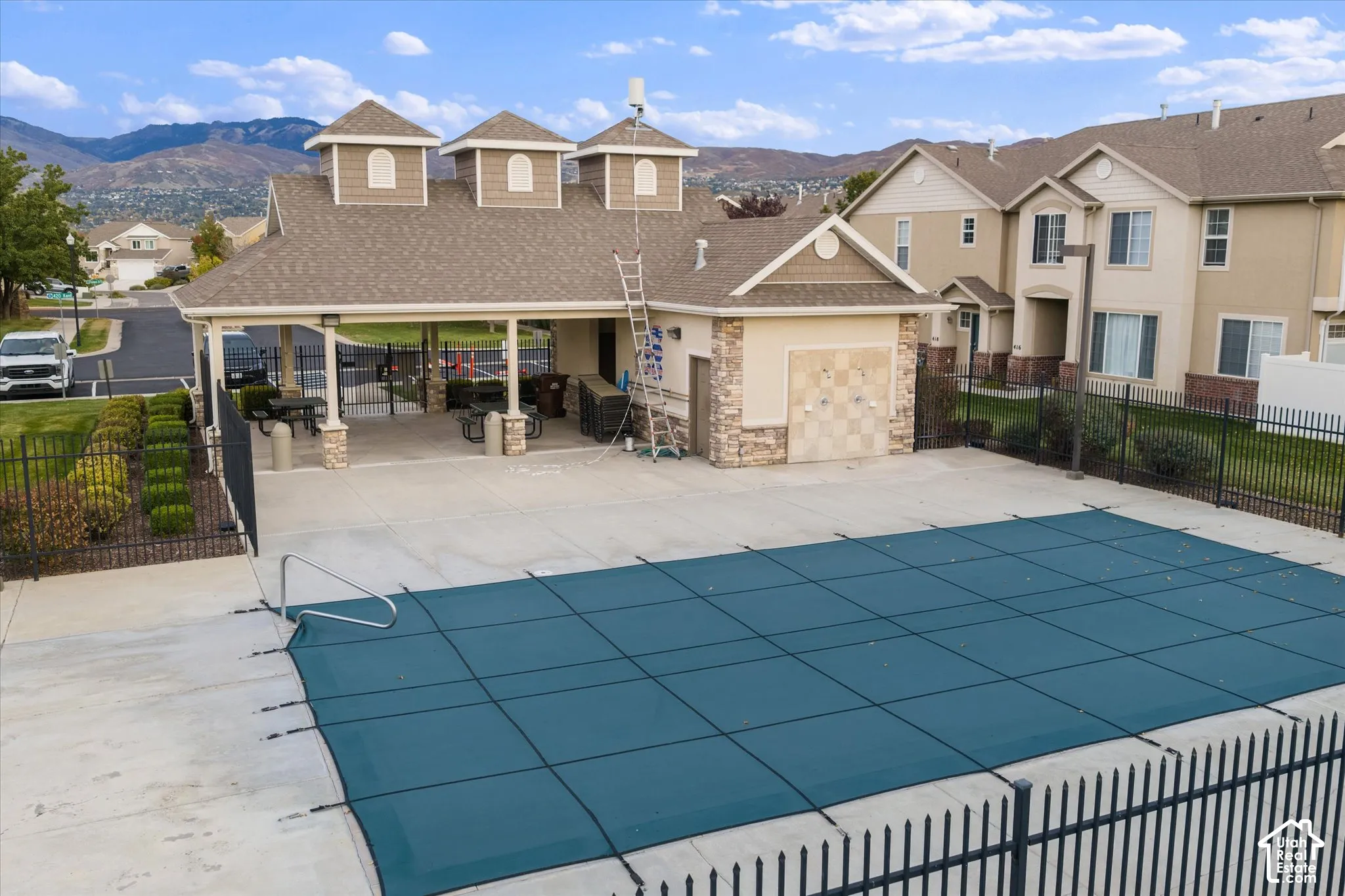 Covered pavilion with stone pillar accents, swimming pool with safety cover, metal perimeter fencing, and concrete decking
