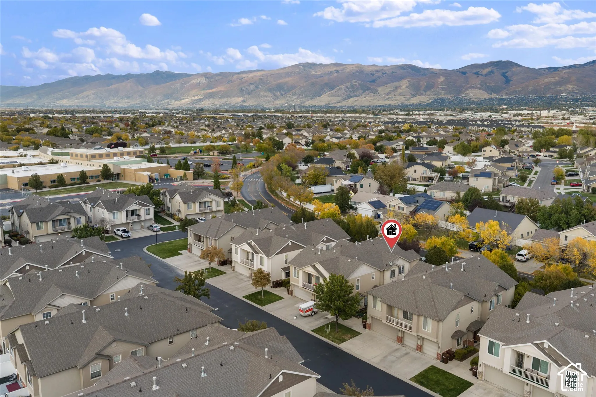 Aerial perspective of residential community featuring multi-level dwellings with pitched roofs, asphalt driveways, and expansive mountain range backdrop