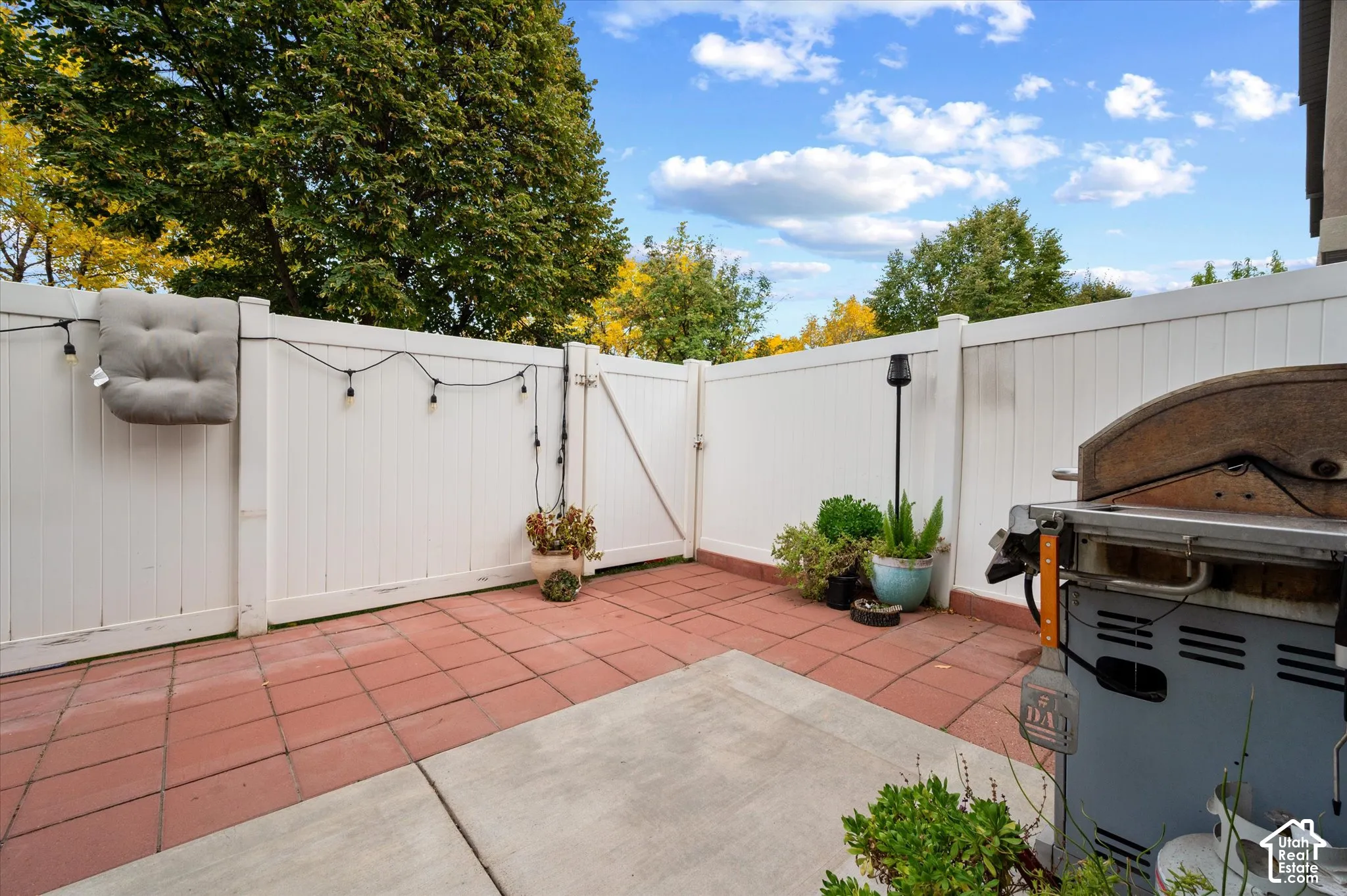 Private patio featuring red tile flooring, a central concrete inlay, and a solid white vinyl privacy fence