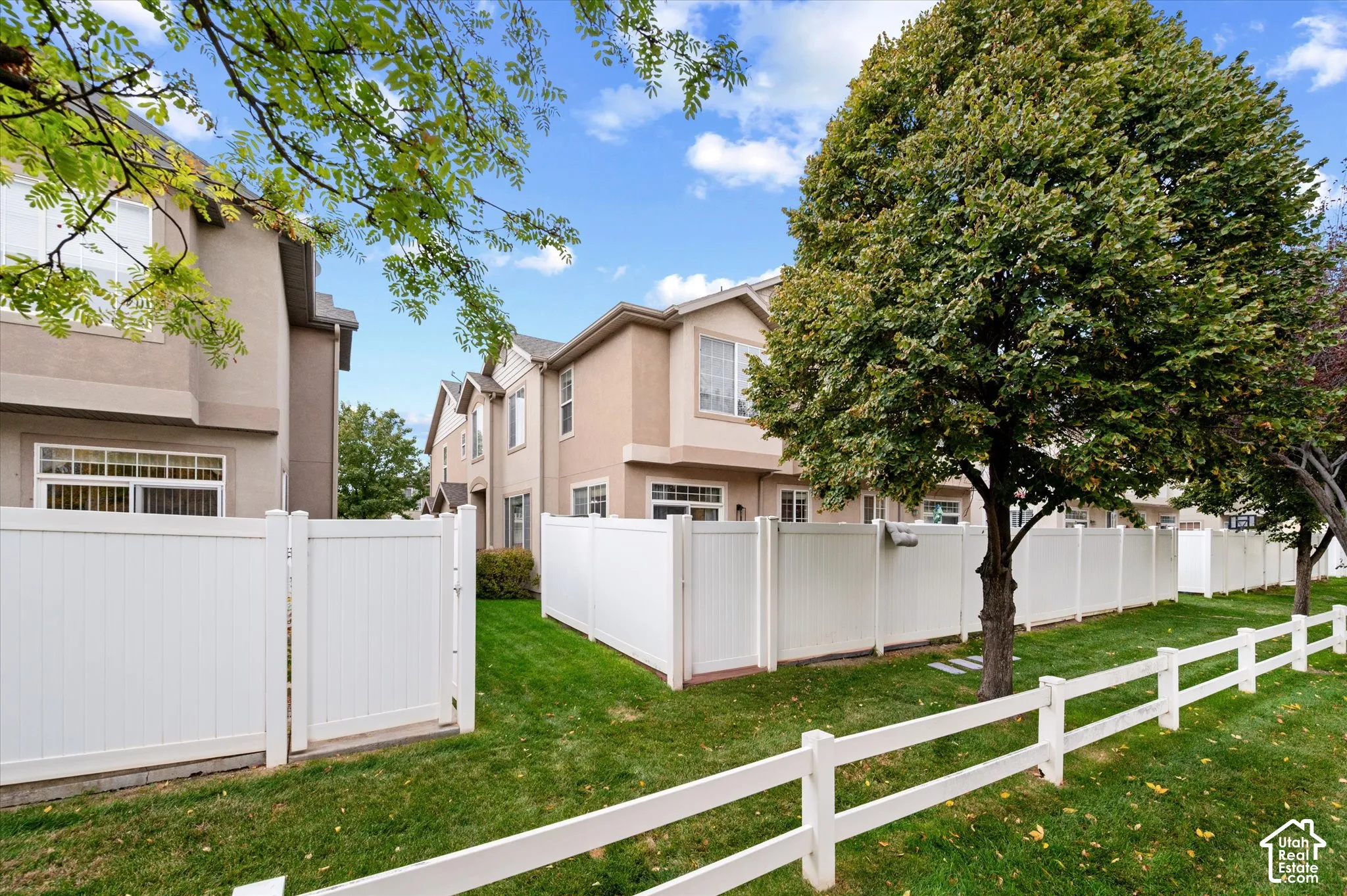 Multi-level exterior featuring stucco siding, white vinyl privacy fencing, post-and-rail perimeter fencing, manicured lawn, and mature trees