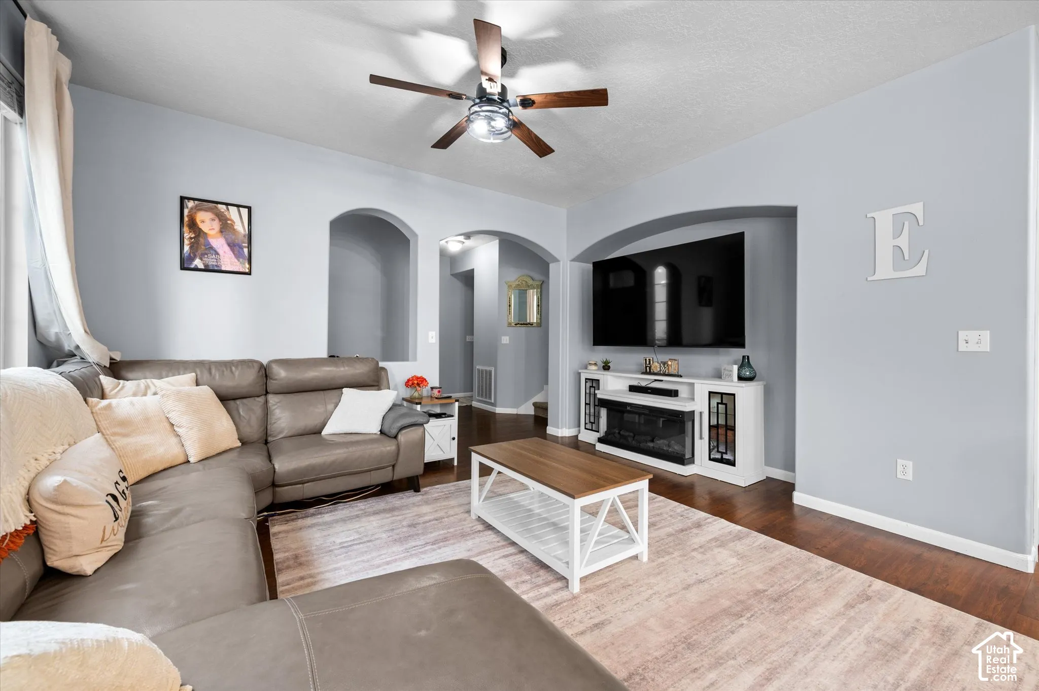 Living area featuring wood-finish flooring, recessed wall niche, arched interior doorways, and a ceiling fan with integrated lighting
