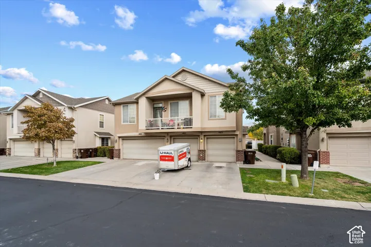 Two-story residence featuring a multi-toned stucco and siding exterior, an attached multi-car garage, and a recessed upper-level balcony with white railings