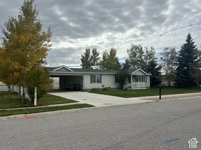 Single-story residence featuring light-toned horizontal siding, a concrete driveway, an attached carport, and a front porch with white railing