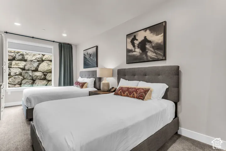 Neutral-toned room featuring recessed lighting, carpeting, and a large picture window showcasing a natural stone retaining wall exterior