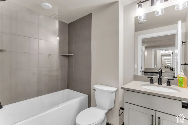 Bathroom featuring a vanity with a solid-surface countertop, rectangular undermount sink, and matte black hardware, paired with a glass-enclosed bathtub featuring large-format tile wall surround and integrated shelving