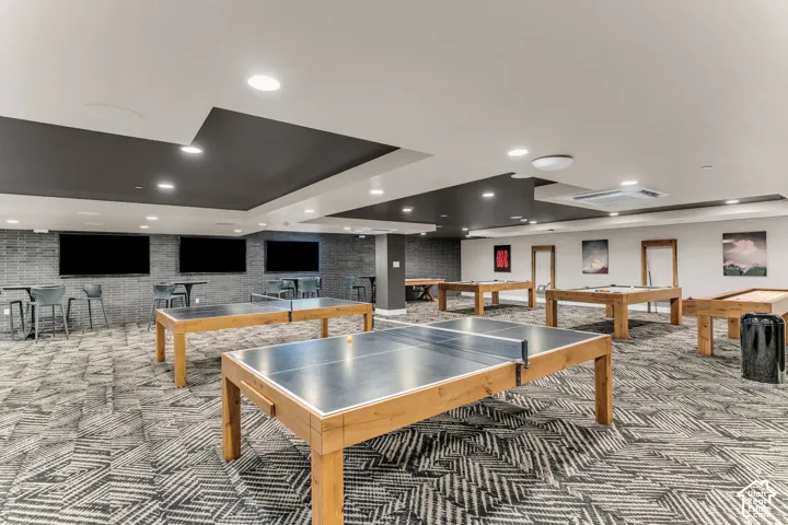 Large-format room featuring recessed ceiling lighting, a multi-tiered soffit with dark-toned architectural accents, patterned carpeting, and integrated wall-mounted display screens