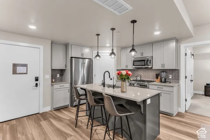 Kitchen featuring gray shaker-style cabinetry, quartz countertops, a central island with a matte black faucet, stainless steel appliances, and wood-finish flooring