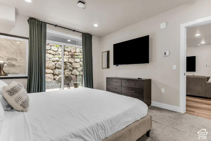 Neutral-toned bedroom featuring recessed lighting, wall-to-wall carpeting, and a sliding glass door providing exposure to a stone retaining wall