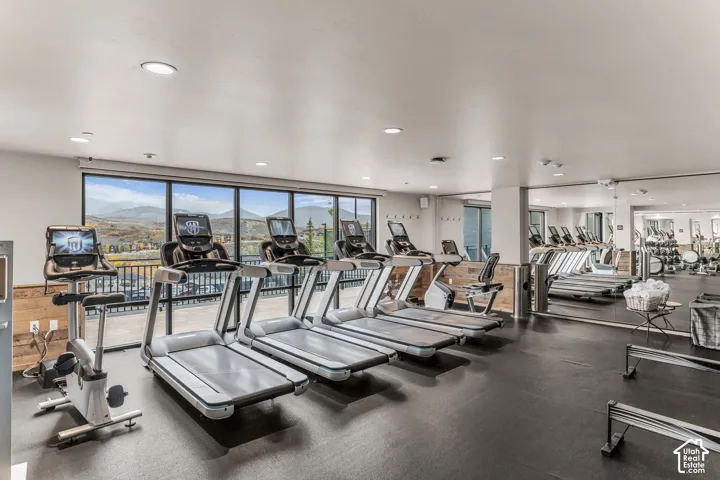 Fitness center featuring floor-to-ceiling windows, mountain scenery, wall-to-wall mirrors, recessed lighting, and rubberized flooring
