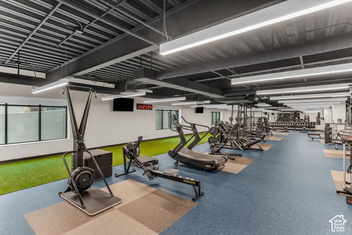 Open-concept fitness space featuring high ceilings with exposed structural beams, LED linear lighting, synthetic turf flooring, and wall-to-wall mirrors