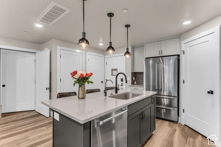 Kitchen island with light-toned countertop, stainless steel appliances, dark cabinetry, wood-finish flooring, and pendant lighting