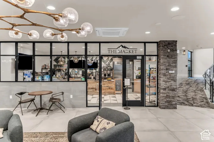 Retail space featuring large-format ceramic floor tiles, a decorative stone pillar, a branching multi-bulb statement chandelier, and an industrial-style glass storefront with black metal framing